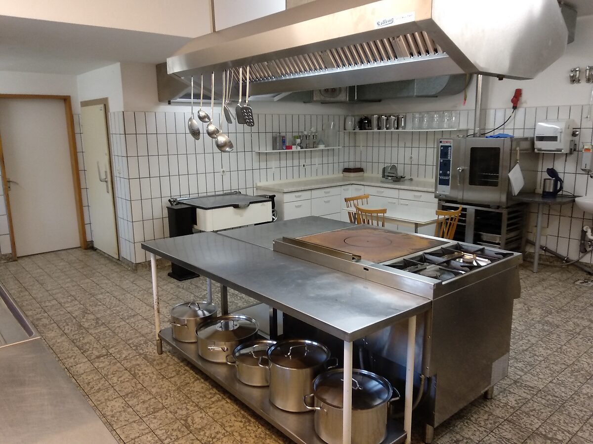 Die Großküche mit Kochinsel, großen Töpfen und hängenden Kellen