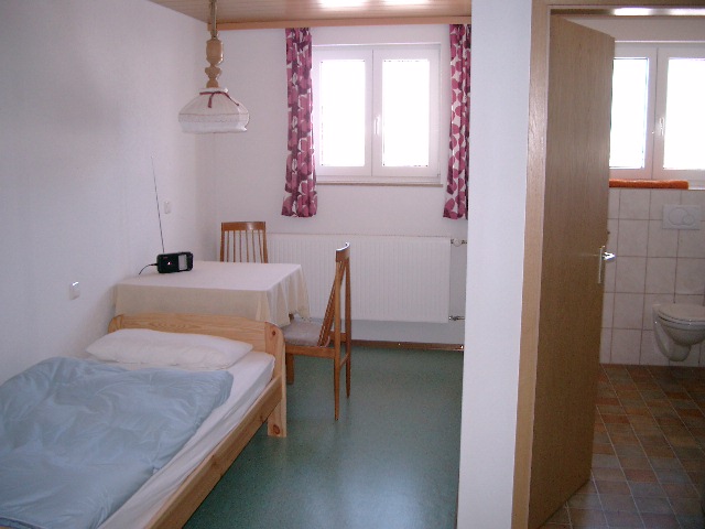 Begleiterzimmer mit Einzelbett, Tisch und angrenzendem WC